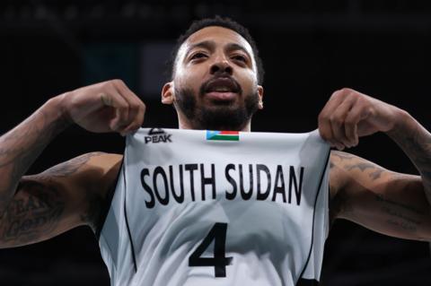 Carlik Jones uses both hands to pinch his jersey and hold it up so the name of South Sudan is prominent underneath his chin