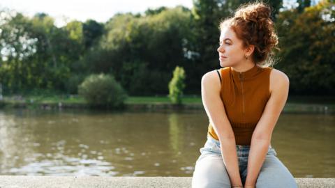 Woman sat on wall next to river 