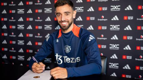 Manchester United midfielder Bruno Fernande smiles as he puts pen to paper on a new contract