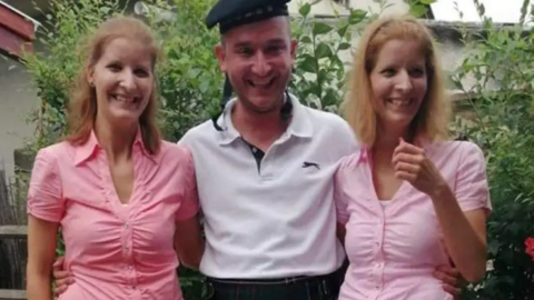 Henrietta and Eliza Huszti standing either side of their brother. Both sisters have brown, shoulder-length hair and are wearing pink shirts. Their brother is in the middle and is wearing a white polo shirt and dark hat. 