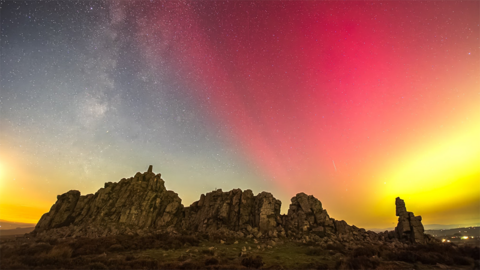 Northern Lights over the Stiperstones in Shropshire. Sheets of red and yellow appear in the sky over a rocky hilltop crag on an otherwise clear night