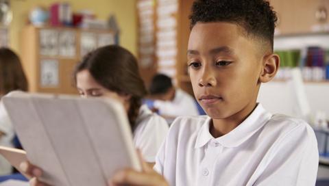 A boy in a school classroom looking at a tablet during class.