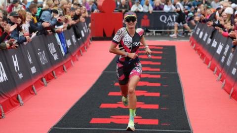 Crowds line the red and black running route with a single runner in mid pace 