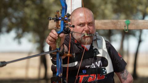 Shaun Anderson lines up a shot using a blue bow with a trigger release held in his mouth