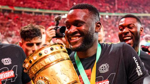 Victor Boniface smiles as he wears a medal around his neck and holds the German Cup trophy during a victory celebration for Bayer Leverkusen