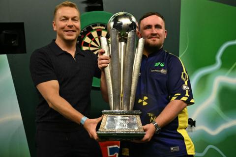 Luke Littler holding the 2025 PDC World Darts Championship with Sir Chris Hoy