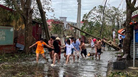 More than a dozen people wade through flood waters and use ropes to remove fallen trees following the impact of Typhoon Yagi in Hai Phong in northern Vietnam