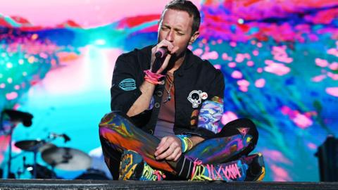Chris Martin sitting on a stage singing
