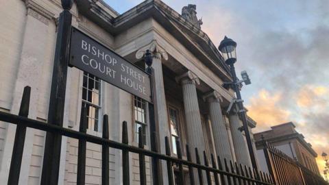 The front of Londonderry Court house,  including four big concrete pillars, as seen through the railings on the outside of the building.