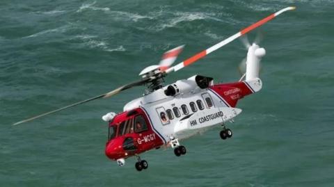 A red and white HM Coastguard helicopter flying over the sea