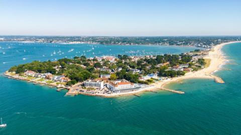 An aerial shot of Sandbanks, a built-up piece of land in the sea. Several groynes made from large rocks can be seen protruding from the beaches into the sea.