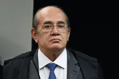 Gilmar Mendes é um homem branco, de meia idade, com óculos de grau quadrados, vestindo uma camisa branca, com gravata azul sob paletó escuro.