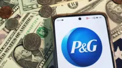 Celuar com logo da Procter & Gamble perto de notas e moedas de dólar