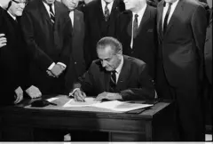 Lyndon Johnson assinando papel, rodeado por pessoas