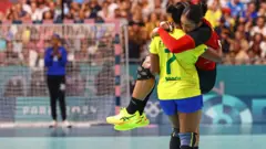 Tamires Araujo, do Brasil, carrega nos braços a rival Albertina Kassoma, de Angola, durante uma partida de handebol 