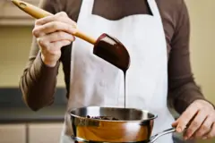 Fotografia colorida mostra uma pessoa branca levantando uma espátula com chocolate derretido em uma panela