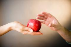 Mão feminina oferece maçã vermelha a mão masculina