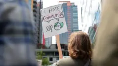 Mulher protestando do lado de fora do escritório da Amazon com uma placa que diz: 'Odeio me deslocar até o trabalho'.