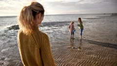 Mulher olhando duas meninas brincando na praia