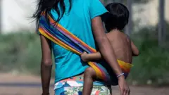 Criança indígena sendo carregada pela mãe