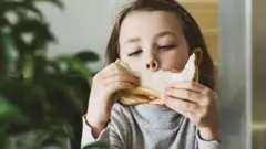 Menina comendo sanduíche de pão de forma branco