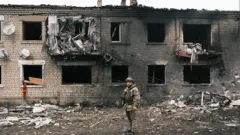 Um soldado ucraniano inspecionando um edifício destruído em Vovchansk