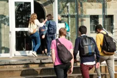 Estudantes de costas caminhando em direção a entrada de instituição