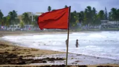 Foto mostra uma bandeira vermelha em uma praia.