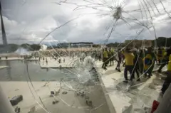 Vidraça do Palácio do Planalto quebrada e manifestantes ao fundo