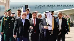 Lula e comitiva brasileira com autoridades da Arábia Saudita. Avião da FAB ao fundo.