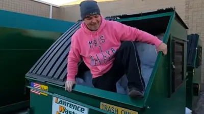 Homem branco com moletom rosa saindo de uma caçamba de lixo