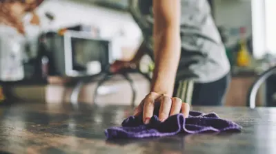 Mão de mulher passando pano em uma mesa de cozinha.