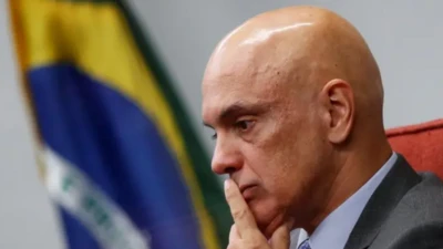 Alexandre de Moraes com o dedo indicador sobre os lábios, aparentando preocupação