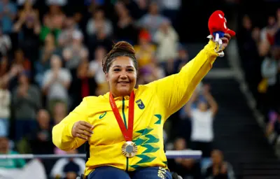 Mulher em cadeira de rodas de pele morena com medalha de ouro no peito celebra vitória 