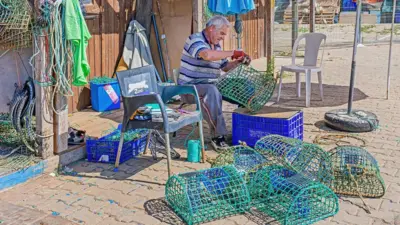 Pescador remendando armadilha para polvos no Algarve, em Portugal