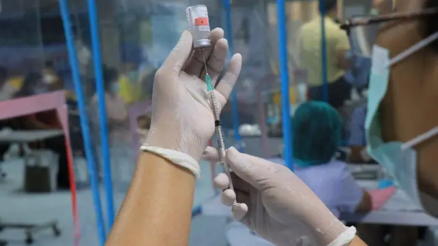 Mão segurando seringa e retirando líquido de frasco de vacina