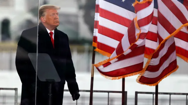 Trump com um casaco escuro perto da bandeira dos EUA