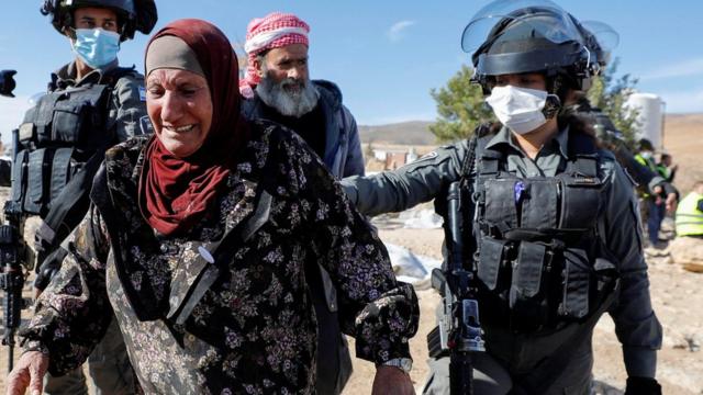 Mujer palestina acompañada por las fuerzas de seguridad israelíes, tras la demolición de un edificio en Cisjordania en enero de 2022.