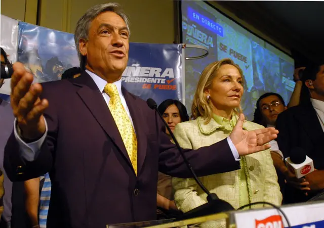 Sebastián Piñera discursando e gesticulando ao lado da esposa, que sorri