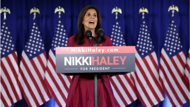 A ex-embaixadora da ONU Nikki Haley durante discurso com bandeiras americanas atrás dela