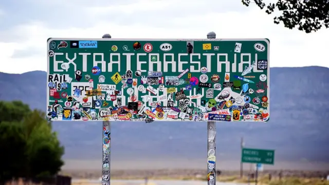 Uma placa de trânsito em que se lê "Extraterrestrial Highway" (em tradução livre, "Estrada para Extraterrestres"), coberta com adesivos, na Rota 375