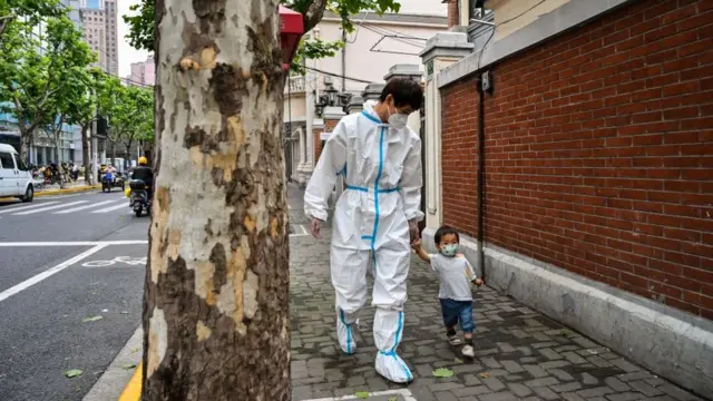 Pessoa com aparato de segurança levando uma criança de máscara pela mão