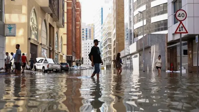 Pessoas caminham pelas ruas alagadas em decorrência das enchentes causadas pelas fortes chuvas em Dubai