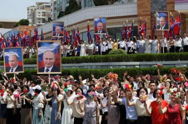 Pessoas balançam flores em rua enfeitada com cartazes de Putin