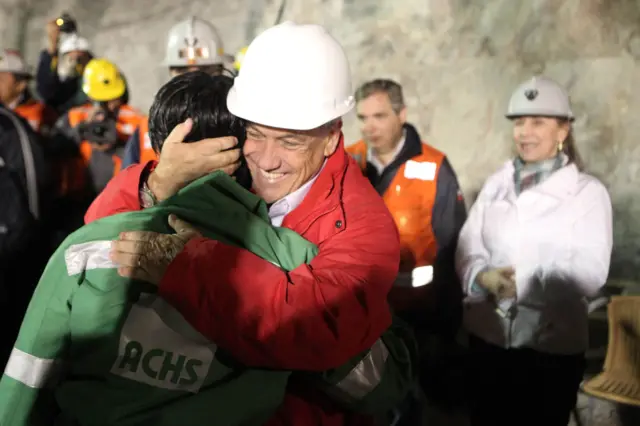 Com capacete, Sebastián Piñera abraça mineiro, que está de costas 