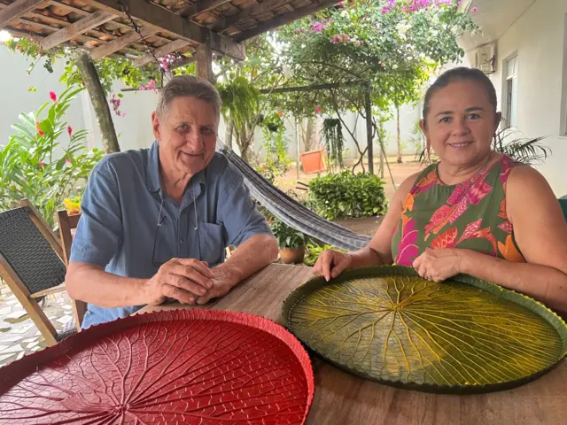 Casal sorrindo em frente a mesa, sobre a qual estão jogos americanos