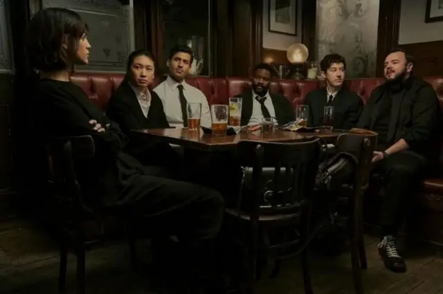 Cena da série da Netflix, em que os cientistas aparecem reunidos em uma mesa de bar