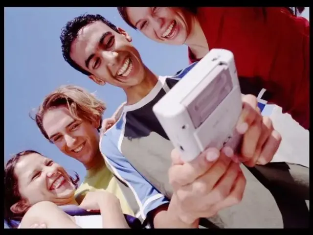 Quatro jovens sorrindo e olhando Gameboy 