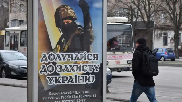 Homem passando por um outdoor mostrando um cartaz de recrutamento com um soldado nele