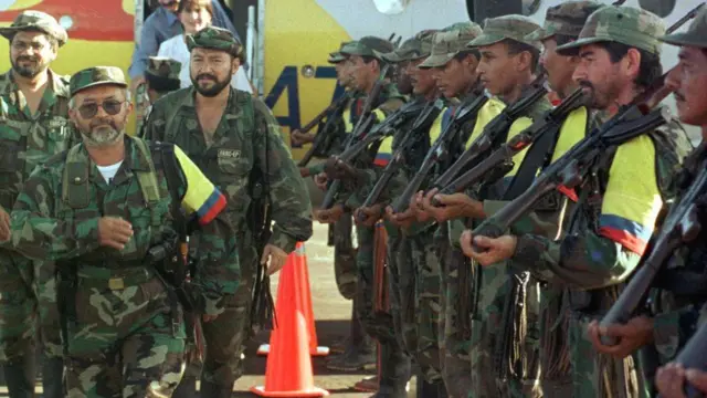 Homens com roupas militares, alguns segurando grandes armas